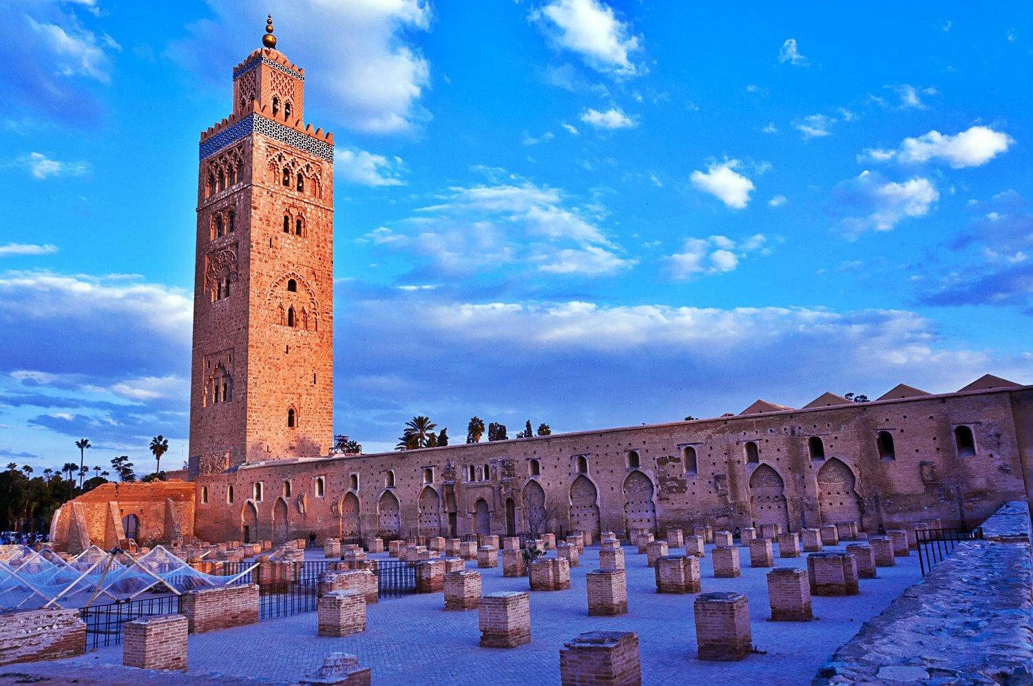Exterior view of the iconic Koutoubia Mosque against a clear blue sky, showcasing intricate architectural details and towering minaret.